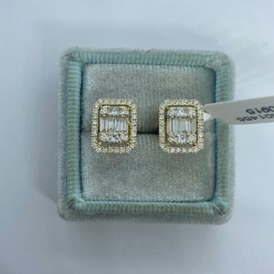 May include: A pair of gold earrings with a rectangular shape and a cluster of small diamonds surrounding a larger baguette-cut diamond in the center.