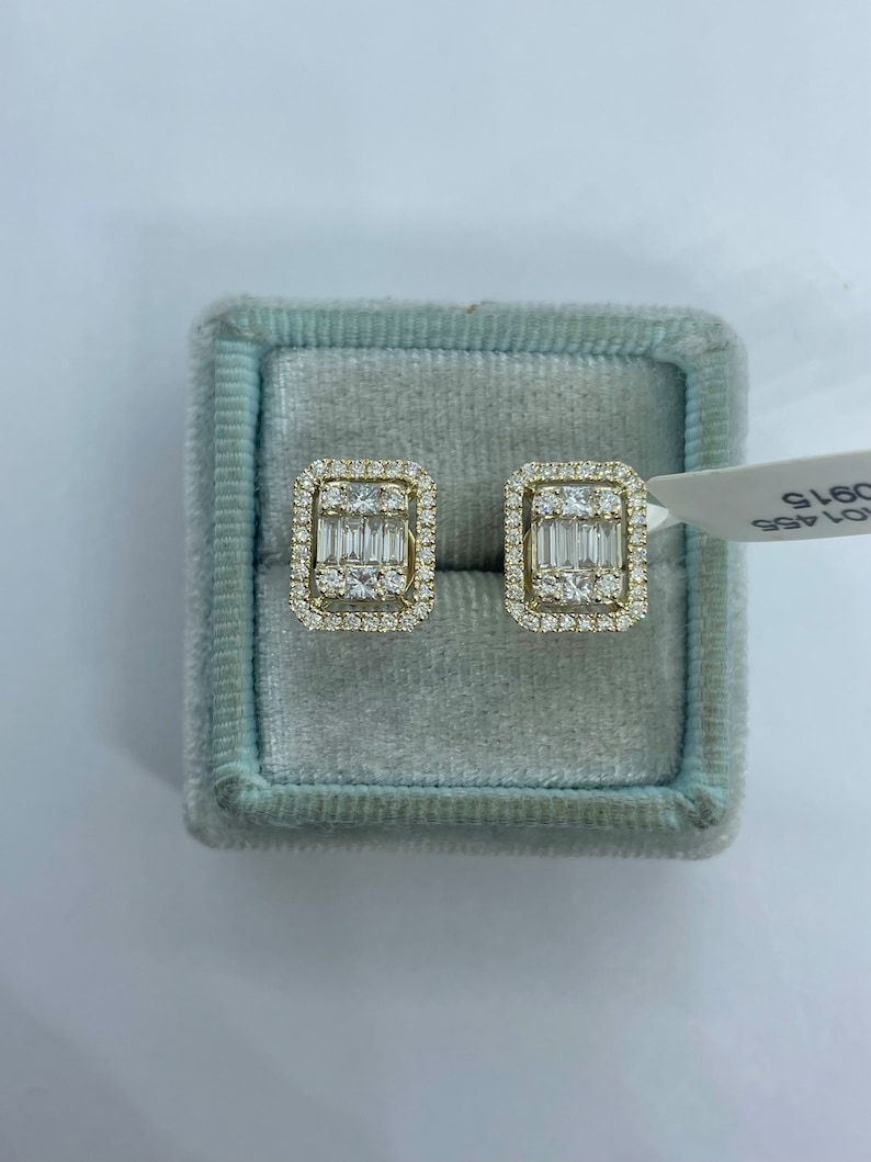 May include: A pair of gold earrings with a rectangular shape and a cluster of small diamonds surrounding a larger baguette-cut diamond in the center.