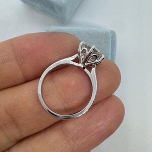 May include: A silver engagement ring with a large, clear gemstone. The ring has a classic solitaire design with a delicate band and a prong setting. A light blue ring box is in the background.