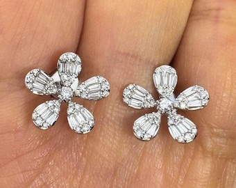 May include: A pair of flower-shaped stud earrings. Each earring features five petals, each adorned with multiple small, sparkling white gemstones. The center of each flower also has a single, larger gemstone.
