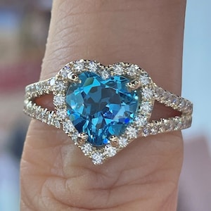 May include: A gold ring with a large heart-shaped blue topaz gemstone surrounded by a halo of smaller diamonds.