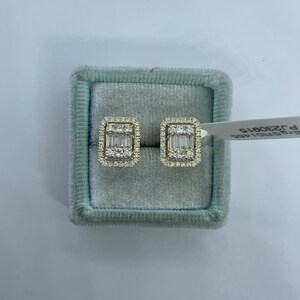 May include: A pair of gold earrings with a rectangular design featuring a cluster of small diamonds. The earrings are displayed in a light blue velvet box.