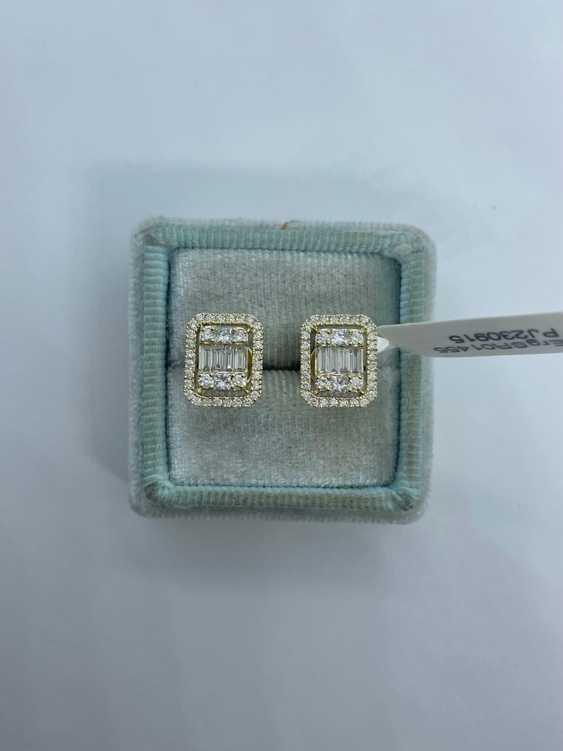 May include: A pair of gold earrings with a rectangular design featuring a cluster of small diamonds. The earrings are displayed in a light blue velvet box.