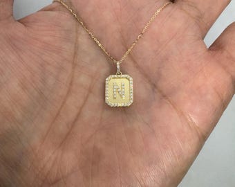 May include: A gold-toned necklace featuring a rectangular pendant with a central letter N. The pendant is bordered by small, clear, sparkling stones and hangs from a delicate gold-toned chain, creating a refined and classic jewelry piece.