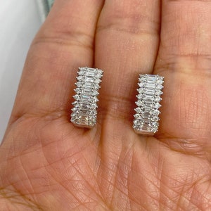 May include: A pair of silver hoop earrings with a row of baguette-cut diamonds on each hoop.