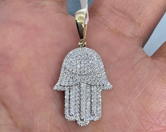 May include: A gold pendant in the shape of a hamsa hand, completely covered in small, sparkling diamonds.