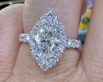 Puede incluir: Un anillo de compromiso de diamante de forma de pera con un engaste halo. El anillo está engastado en oro blanco y presenta un halo doble de diamantes más pequeños.