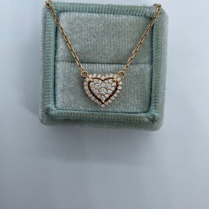 Puede incluir: Un collar de oro con un colgante en forma de coraz&oacute;n con un engaste de pav&eacute; de peque&ntilde;os diamantes. El collar se muestra en una caja de terciopelo azul claro.