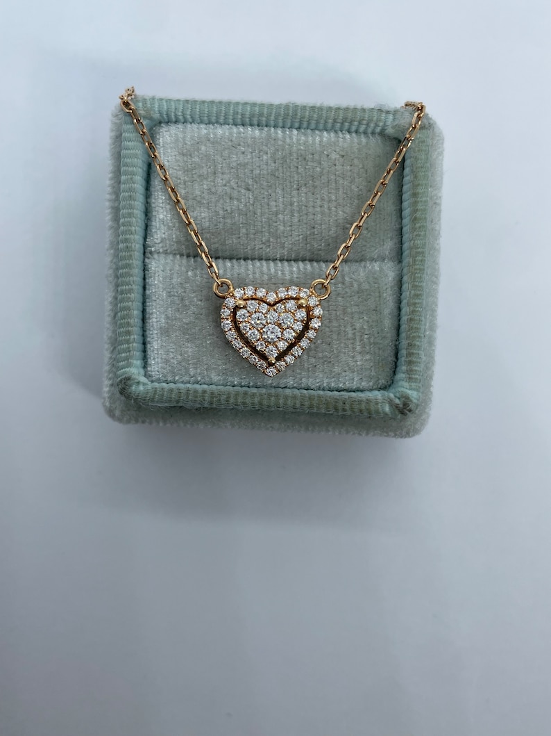 Puede incluir: Un collar de oro con un colgante en forma de coraz&oacute;n con un engaste de pav&eacute; de peque&ntilde;os diamantes. El collar se muestra en una caja de terciopelo azul claro.