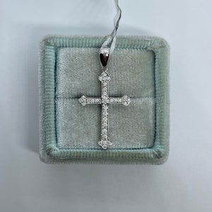 May include: A silver cross pendant with a white stone setting. The pendant is in a light blue velvet box.