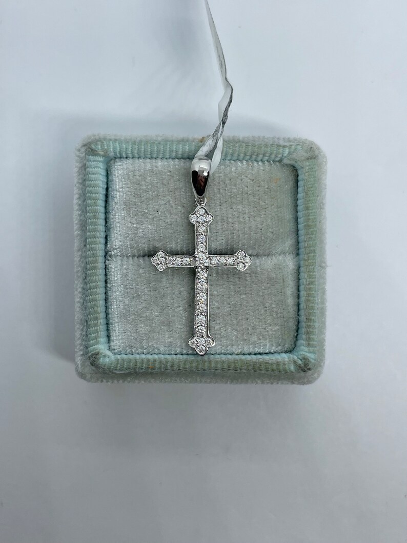 May include: A silver cross pendant with a white stone setting. The pendant is in a light blue velvet box.