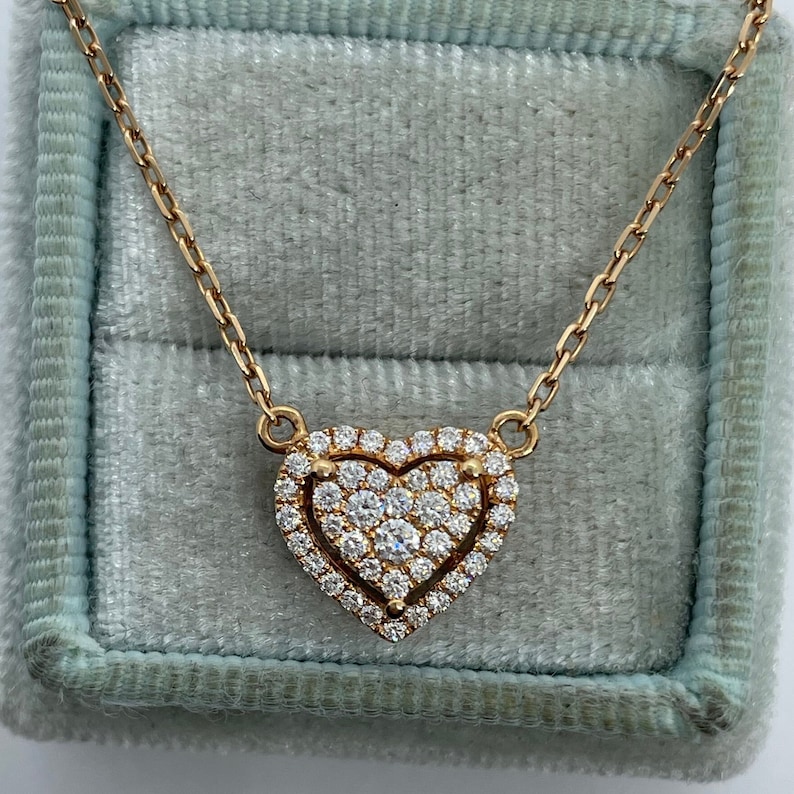Puede incluir: Un collar de cadena de oro con un colgante en forma de coraz&oacute;n engastado con peque&ntilde;os diamantes. El colgante tiene una doble capa de diamantes, con una forma de coraz&oacute;n m&aacute;s peque&ntilde;a en el centro.