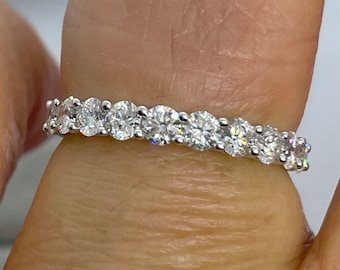 May include: A silver ring with a continuous row of oval-cut, clear gemstones. The gemstones are set closely together, creating a sparkling band. The ring is shown on a finger, highlighting the design and brilliance of the stones.
