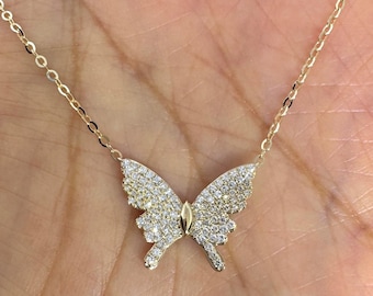 May include: A gold-colored butterfly pendant necklace. The butterfly design is encrusted with small, sparkling white stones. The necklace chain is delicate and also gold-colored.