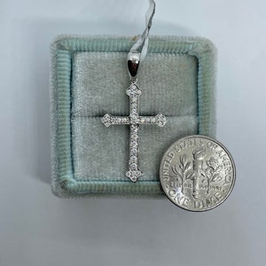 May include: A silver cross pendant with small clear stones set into the metal. The cross is in a blue velvet box next to a US dime for size comparison.