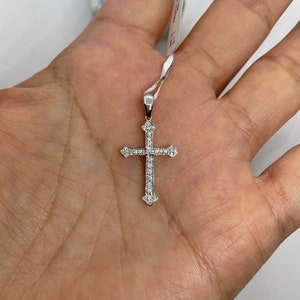May include: A silver cross pendant with small clear stones set into the metal. The cross is on a white background.