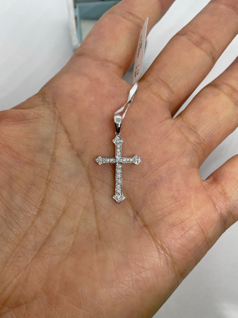 May include: A silver cross pendant with small clear stones set into the metal. The cross is on a white background.