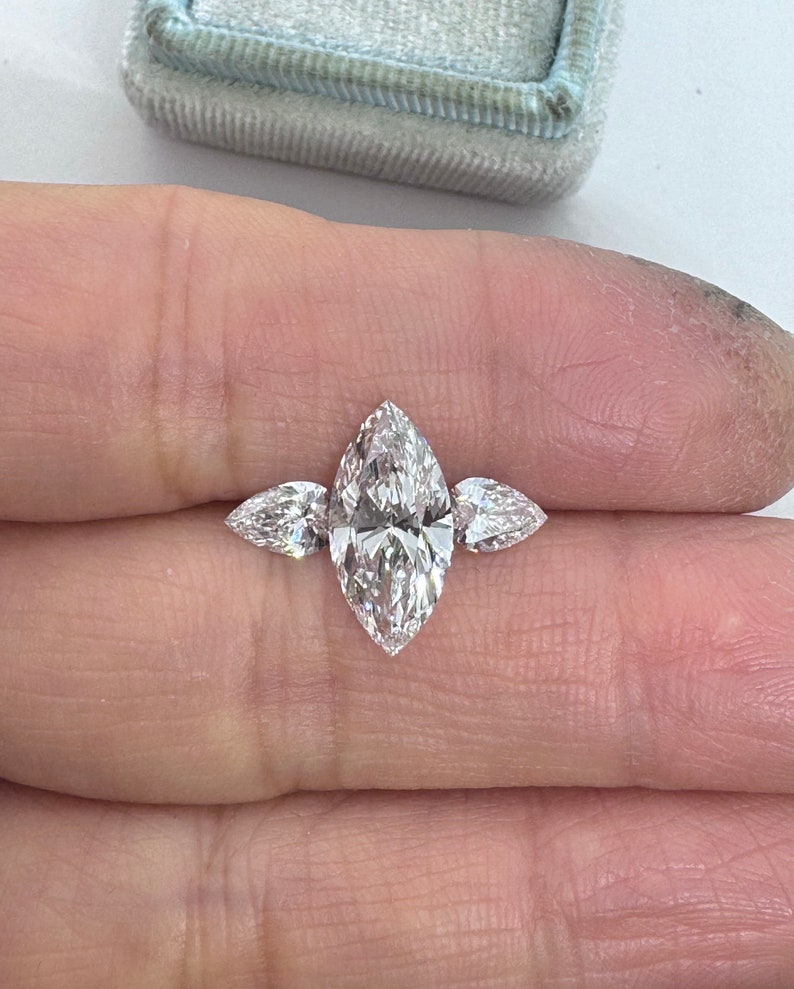 May include: A three-stone marquise diamond engagement ring with a large center stone and two smaller side stones.