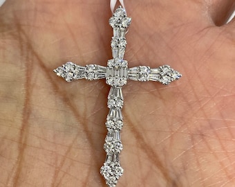 May include: A diamond cross pendant with a white metal setting. The cross is adorned with numerous round and baguette-cut diamonds, creating a sparkling and elegant design. The pendant is suspended from a white cord.