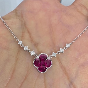 May include: A delicate silver chain necklace with a cluster of five red rubies set in a clover shape. The necklace is adorned with small diamonds along the chain.