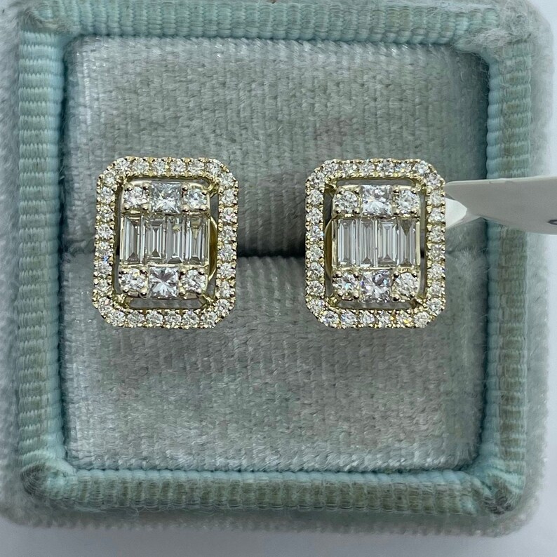May include: A pair of gold earrings with a square shape and a halo of small diamonds surrounding a larger center diamond. The center diamond is surrounded by a row of baguette diamonds.