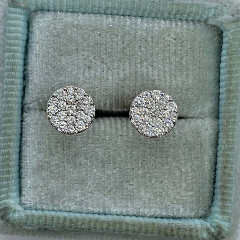 May include: A pair of silver stud earrings with a round design featuring a cluster of small, clear diamonds.