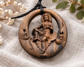 May include: A circular dark brown wooden pendant featuring a detailed hand-carved figure of a seated deity in the center. The pendant is suspended from a black cord and displays intricate relief carvings of clouds and flowing robes.