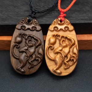 May include: Two wooden pendants featuring a monkey design. The pendants are carved from dark wood and light wood. The monkey is holding a peach in its hand. The pendants are suspended from black and red cords.