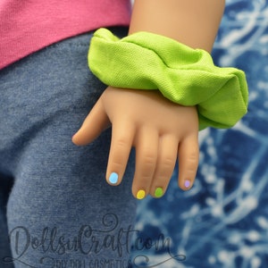 Puede incluir: Una mano de mu&ntilde;eca con esmalte de u&ntilde;as de colores. Las u&ntilde;as est&aacute;n pintadas en tonos de azul, amarillo y verde. La mano lleva una goma el&aacute;stica verde.