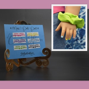 Puede incluir: Una tarjeta azul con el texto "Mani/Pedi Pack" y filas de puntos de colores. La tarjeta est&aacute; en un soporte dorado. Se ve una mano de mu&ntilde;eca con las u&ntilde;as pintadas en el fondo.