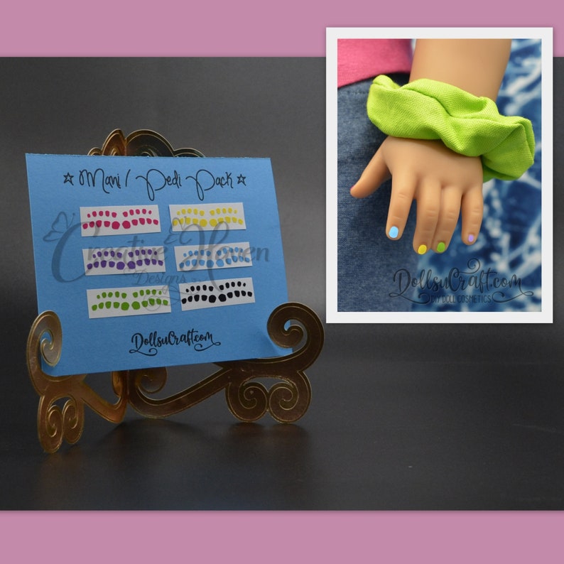 Puede incluir: Una tarjeta azul con el texto "Mani/Pedi Pack" y filas de puntos de colores. La tarjeta est&aacute; en un soporte dorado. Se ve una mano de mu&ntilde;eca con las u&ntilde;as pintadas en el fondo.
