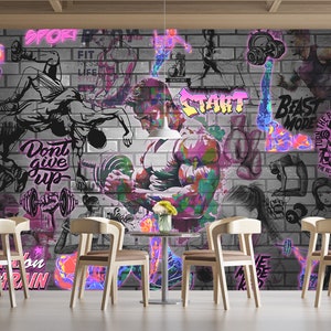 K&ouml;nnte beinhalten: Ein farbenfrohes Graffiti-Wandbild mit einem Hintergrund aus Ziegelmauer. Das Wandbild zeigt Bilder von Menschen, die trainieren, Gewichte heben und motivierende Zitate. Der Text im Wandbild beinhaltet "Sport", "Fit", "Gib nicht auf", "Beast Mode", "Verwandle den Schmerz in Kraft" und "Start".