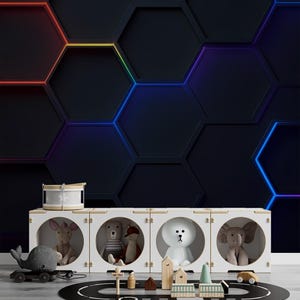 May include: A white toy storage unit with four circular openings, each containing a stuffed animal. A toy drum, a whale on wheels, and a toy road with wooden buildings and cars are in front of the unit. The background is a dark wall with hexagon shapes outlined in rainbow colours.