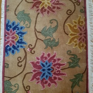 May include: A beige rug with a floral pattern. The flowers are in shades of pink, blue, yellow, and green. The rug has a fringe border.