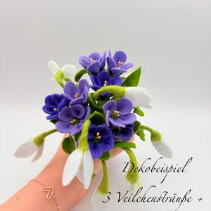 K&ouml;nnte beinhalten: Ein Blumenstrau&szlig; aus Filz mit violetten Veilchen und wei&szlig;en Schneegl&ouml;ckchen. Die Anordnung umfasst gr&uuml;ne Stiele und Bl&auml;tter. Der Text auf dem Bild lautet "Dekobeispiel 3 Veilchenstr&auml;u&szlig;e + 9 Schneegl&ouml;ckchen."