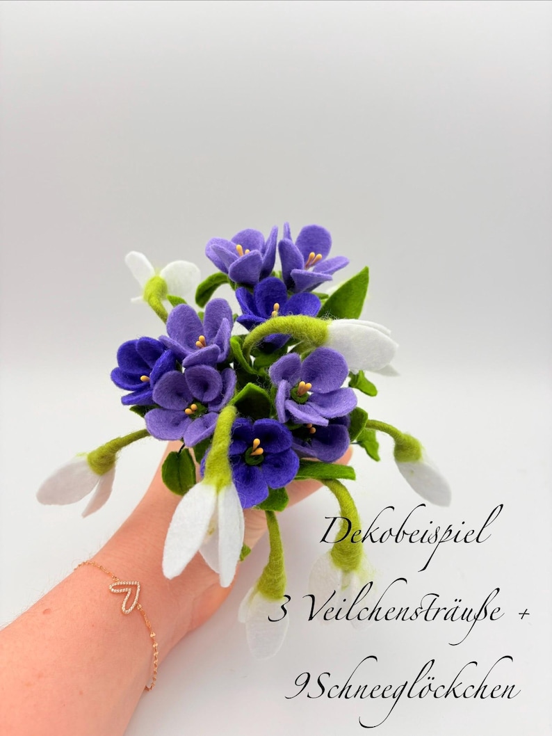 K&ouml;nnte beinhalten: Ein Blumenstrau&szlig; aus Filz mit violetten Veilchen und wei&szlig;en Schneegl&ouml;ckchen. Die Anordnung umfasst gr&uuml;ne Stiele und Bl&auml;tter. Der Text auf dem Bild lautet "Dekobeispiel 3 Veilchenstr&auml;u&szlig;e + 9 Schneegl&ouml;ckchen."