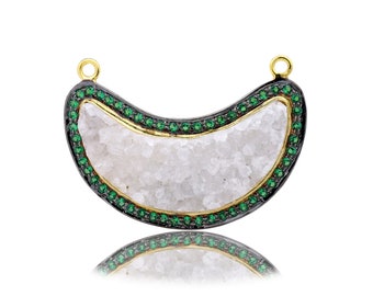 May include: A crescent moon shaped pendant with a white quartz center and a black and gold border. The border is set with small green gemstones.