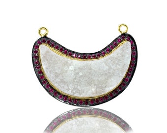 May include: A crescent moon shaped pendant with a white stone center and a black and gold rim. The rim is decorated with small red gemstones.