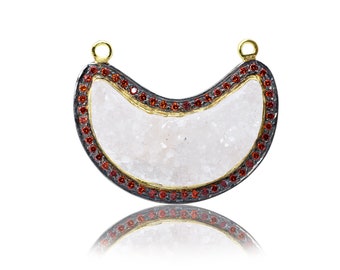 May include: A crescent-shaped pendant with a white quartz center, surrounded by a black border and a row of red gemstones.