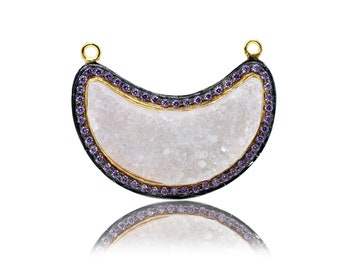 May include: A crescent moon shaped pendant with a white, textured stone set in a black metal frame with a gold trim. The frame is decorated with small purple gemstones.