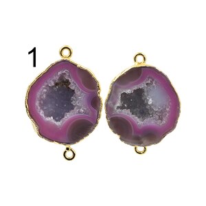 Op de afbeelding: Twee edelsteenhangers met een goudkleurige rand. De hangers zijn een mix van paars, wit en grijs. De edelsteen heeft een geode-achtig uiterlijk. Elke hanger heeft een lus aan de boven- en onderkant om te bevestigen.