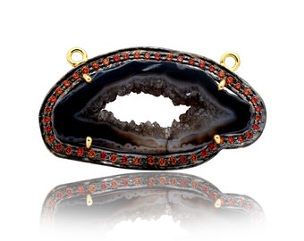 May include: A black agate pendant with a natural crystal formation and a gold-toned metal setting. The pendant is accented with small red gemstones around the edge.