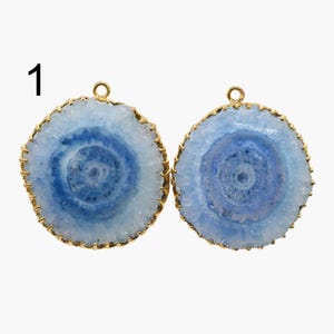 May include: Two round blue and white agate gemstone pendants with gold-toned metal frames. The pendants have a circular design in the center.
