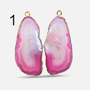 Op de afbeelding: Twee roze agaat plakjes met goudkleurige metalen accenten. De agaat plakjes zijn ovaalvormig en hebben een natuurlijke, organische uitstraling.
