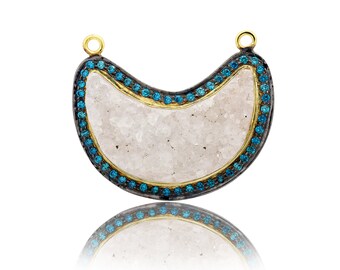 May include: A crescent moon shaped pendant with a white quartz center and a black and gold rim. The rim is decorated with small blue gemstones.