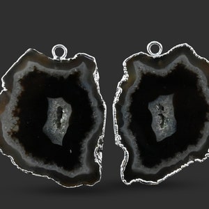 May include: Two black agate slices with silver-toned metal accents and loops for hanging. The agate has a white and grey banded pattern.