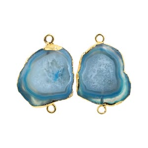 May include: Two blue and white agate gemstone pendants with gold-colored edges and loops. The pendants have a natural, irregular shape and a polished finish. The blue color varies in intensity, creating a layered effect.