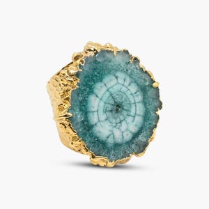 May include: A gold ring featuring a large, round, green and white agate stone. The stone has a swirling pattern and a rough, natural edge.