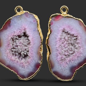 May include: Two pink agate slices with gold trim and a hole at the top. The agate has a white and pink crystal pattern.