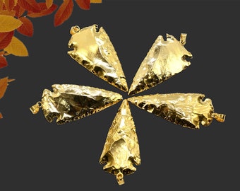 May include: Five gold-colored arrowhead pendants arranged in a star shape against a dark gray background.